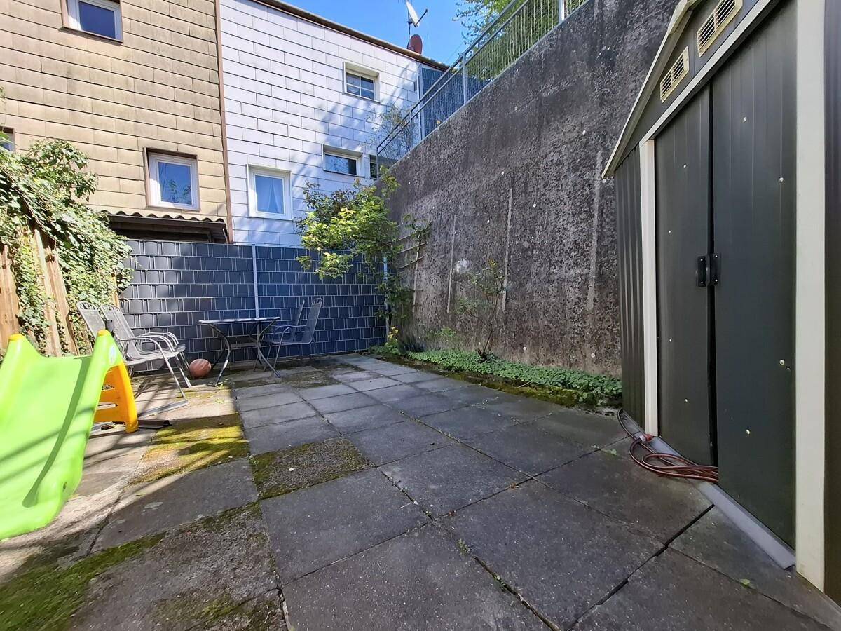 Gepflasterte Terrasse mit Gartenmöbeln, einem Geräteschuppen und einer hohen Mauer.