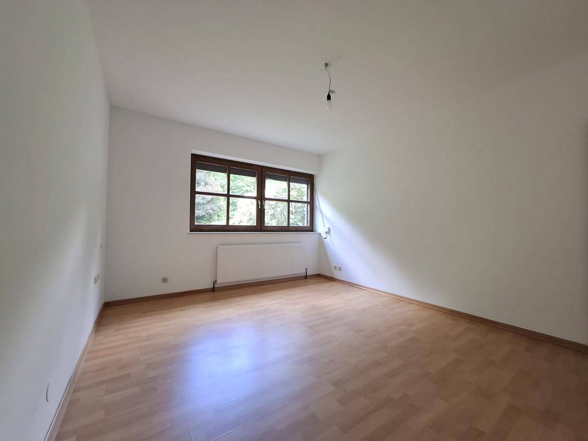 Geräumiges Zimmer mit Parkettboden, großem Fenster und Heizkörper.