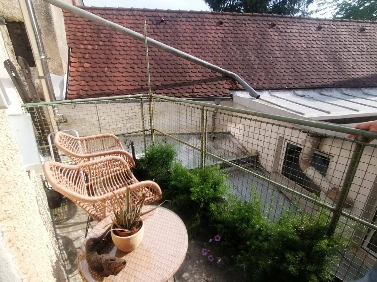Kleiner Balkon mit Korbmöbeln und Pflanzen, mit Blick auf ein rotes Ziegeldach.
