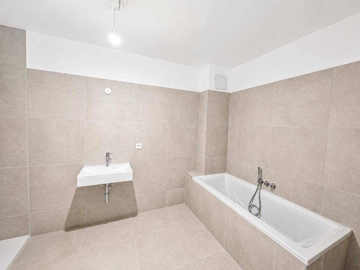 Modernes Badezimmer mit Badewanne, Einzelwaschbecken und beigefarbenen Fliesen.