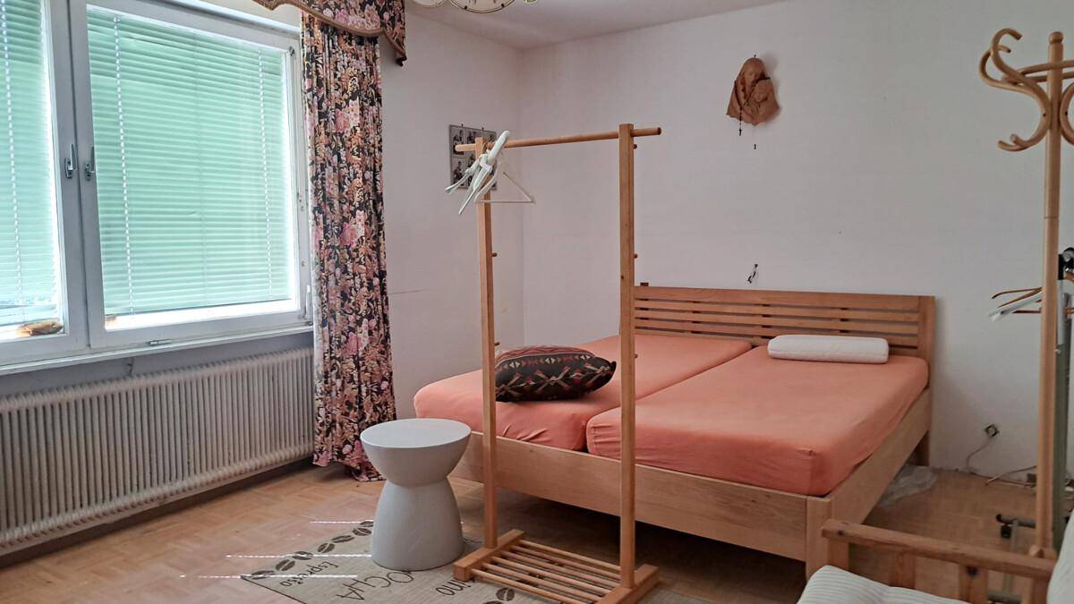 Schlafzimmer mit zwei Einzelbetten, Holzmöbeln und Fenster mit Jalousien, schlicht eingerichtet.