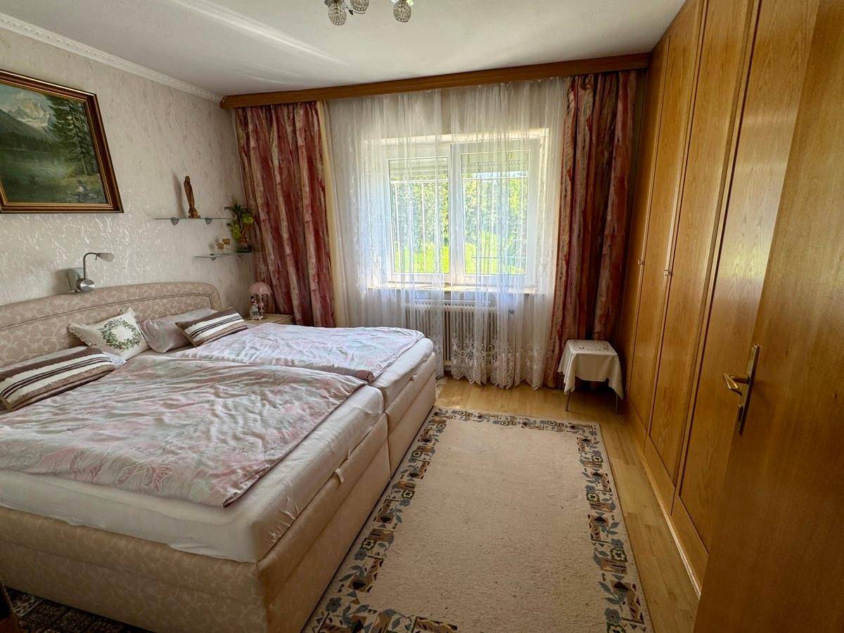 Schlafzimmer mit zwei Einzelbetten, Holzschrank und Fenster mit Blick ins Grüne.