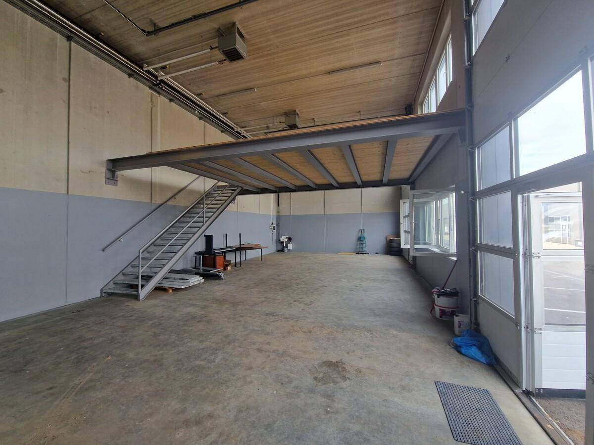 Geräumiger Lagerbereich mit hoher Decke, Betonboden und einer Metalltreppe zur Zwischenebene.