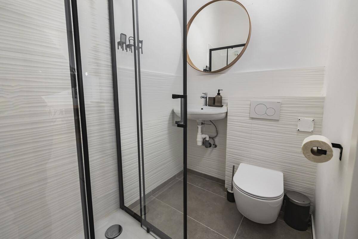 Modernes Badezimmer mit Duschkabine, wandhängendem WC und rundem Spiegel.