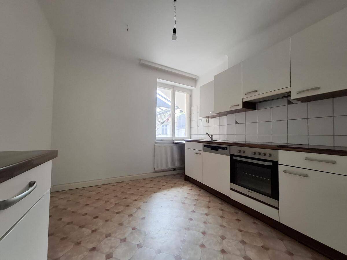 Helle Küche mit weißen Einbauschränken, Herd und Fensterblick, ausgestattet mit Spülmaschine.