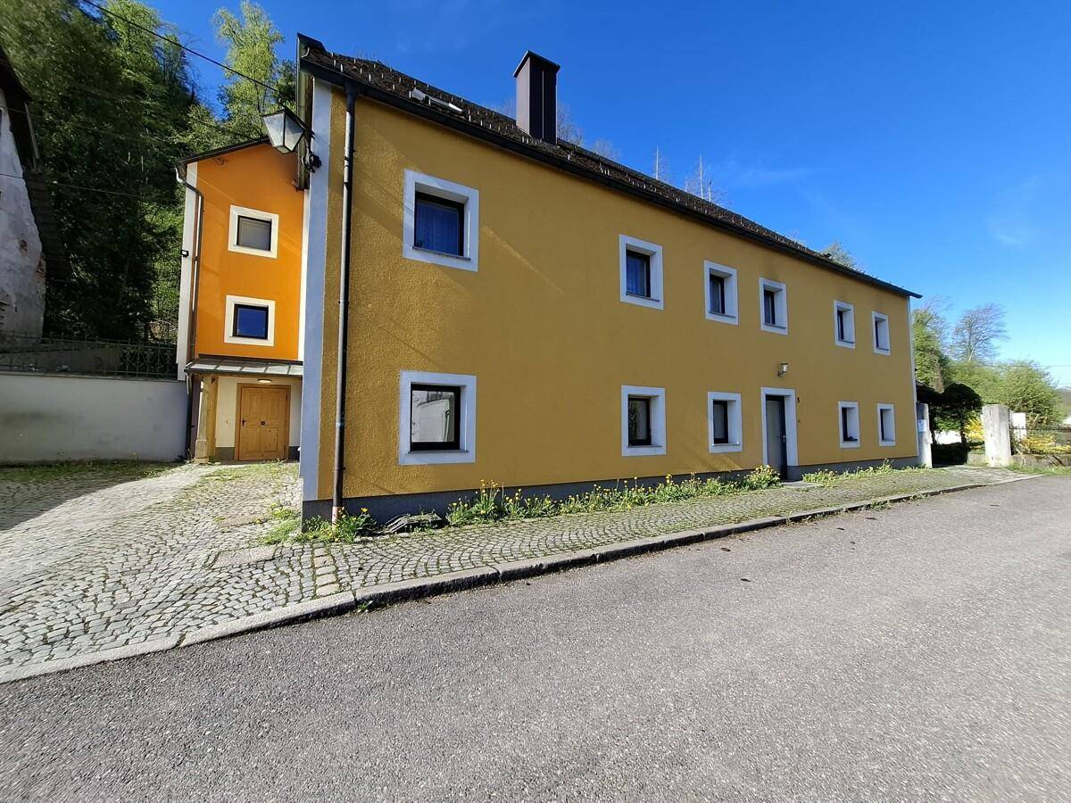 Seitenansicht des gelben Gebäudes mit Straße und gepflegter Umgebung an einem sonnigen Tag.