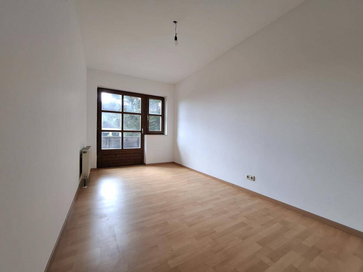 Helles Zimmer mit Parkettboden und Zugang zu einem kleinen Balkon oder Terrasse.