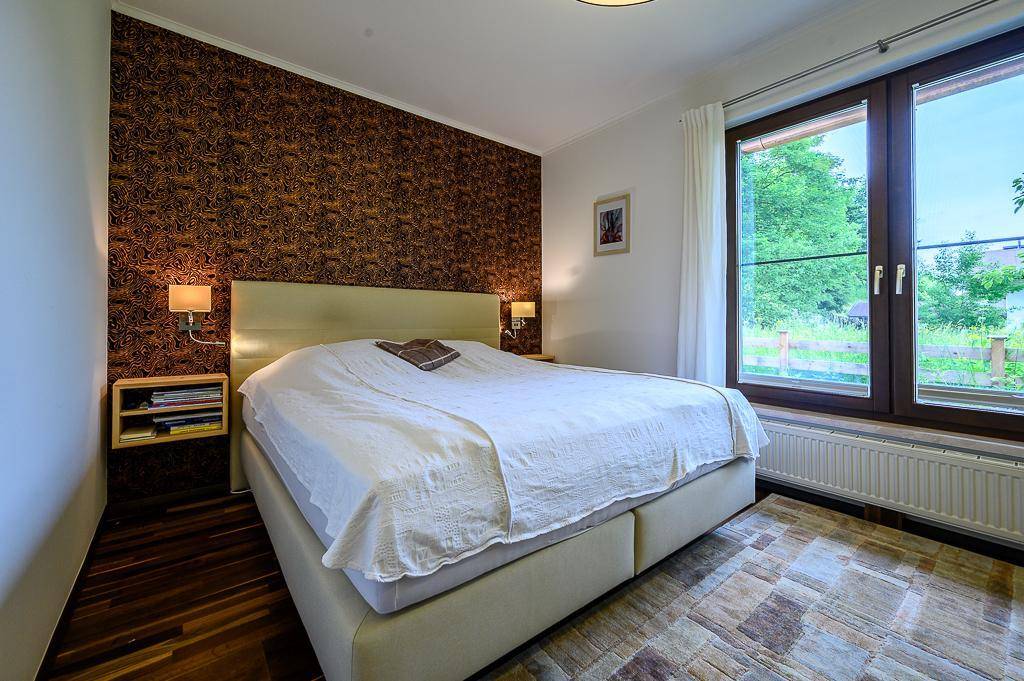 Gemütliches Schlafzimmer mit Doppelbett, gemusterten Tapeten und Fenster zum Garten.