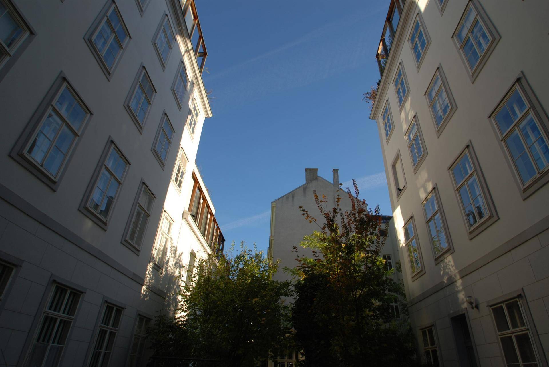 Innenhofansicht mit hohen Gebäuden und Bäumen unter blauem Himmel.