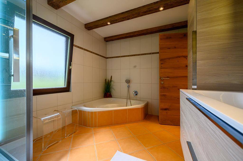 Geräumiges Badezimmer mit Eckbadewanne, Duschkabine und Holzbalken an der Decke.