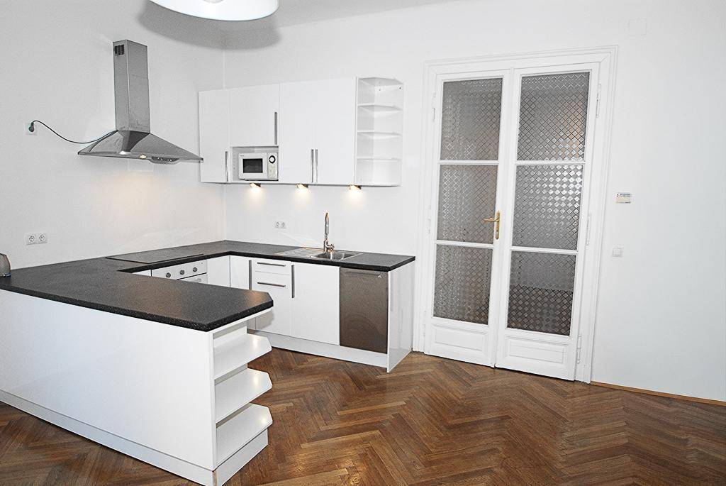 Moderne weiße Einbauküche mit dunkler Arbeitsplatte und Fischgrätparkettboden.
