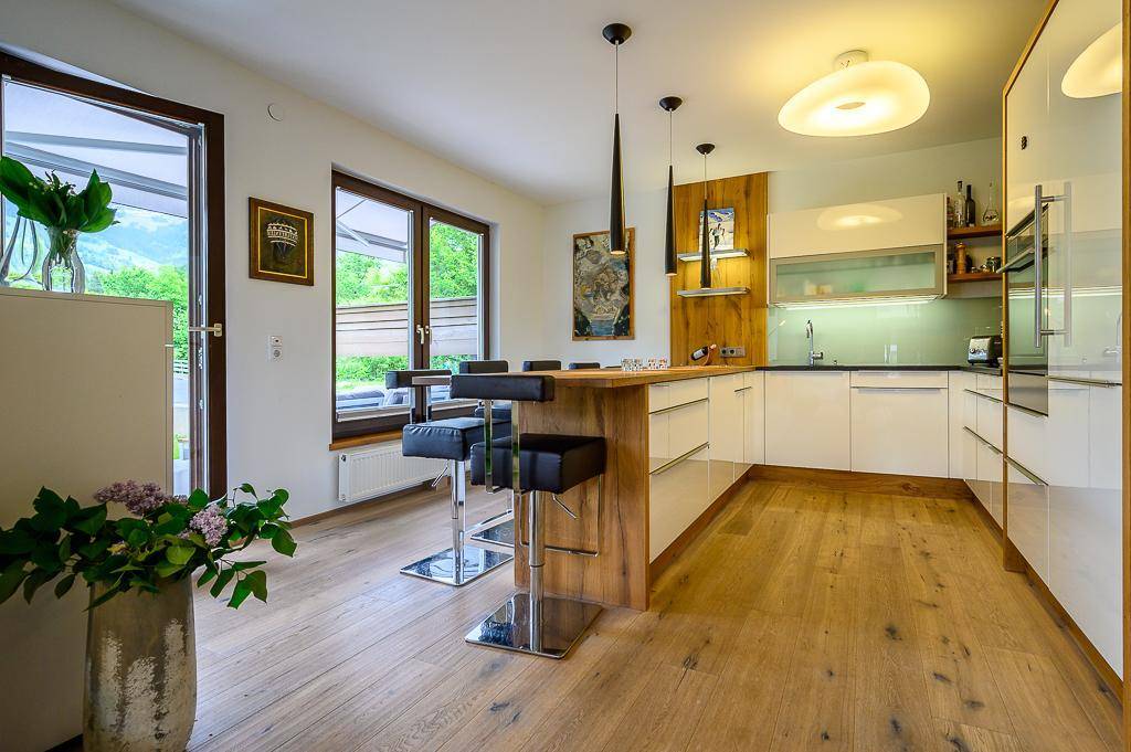 Moderne Küche mit weißen Fronten, Holzakzenten und Bartresen mit Blick ins Grüne.