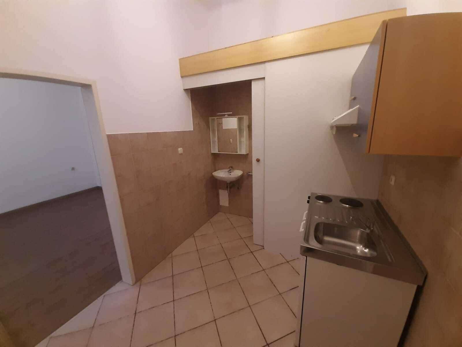 Praktische Küchenzeile in gefliestem Bereich, angrenzend an ein kleines Bad mit Waschbecken.