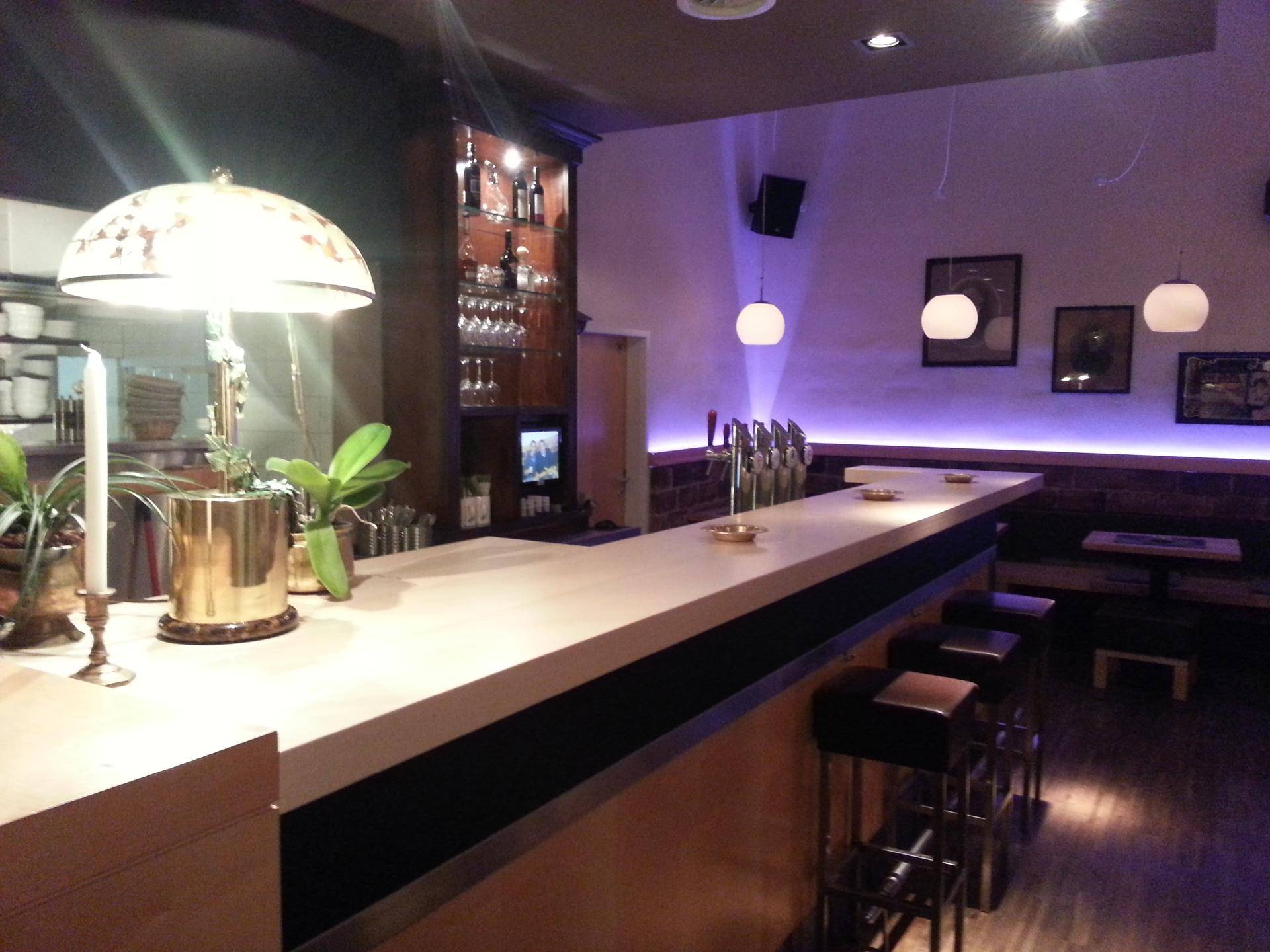 Die Bar bei Nacht, mit beleuchteter Theke und Barhockern, die eine einladende Atmosphäre schaffen.
