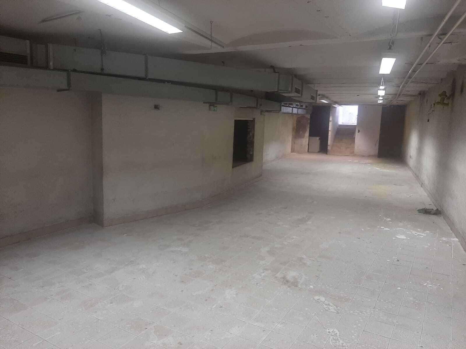 Geräumiger Gewerberaum im Keller mit Fliesenboden und sichtbaren Installationen an der Decke.