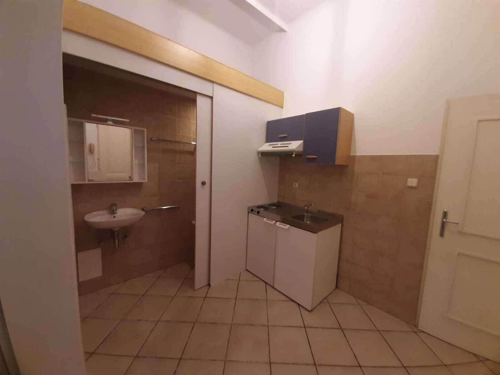Küchenzeile mit Fliesenboden und Blick auf ein kleines Badezimmer mit Waschbecken und Spiegelschrank.