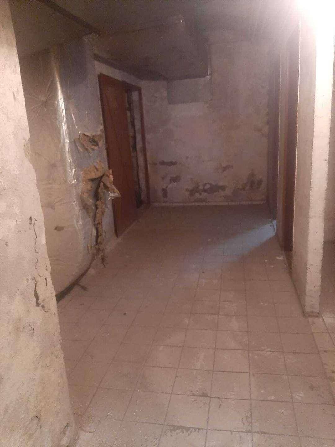Langer Flur im Rohbauzustand mit Fliesenboden und mehreren Türen, die zu weiteren Räumen führen.