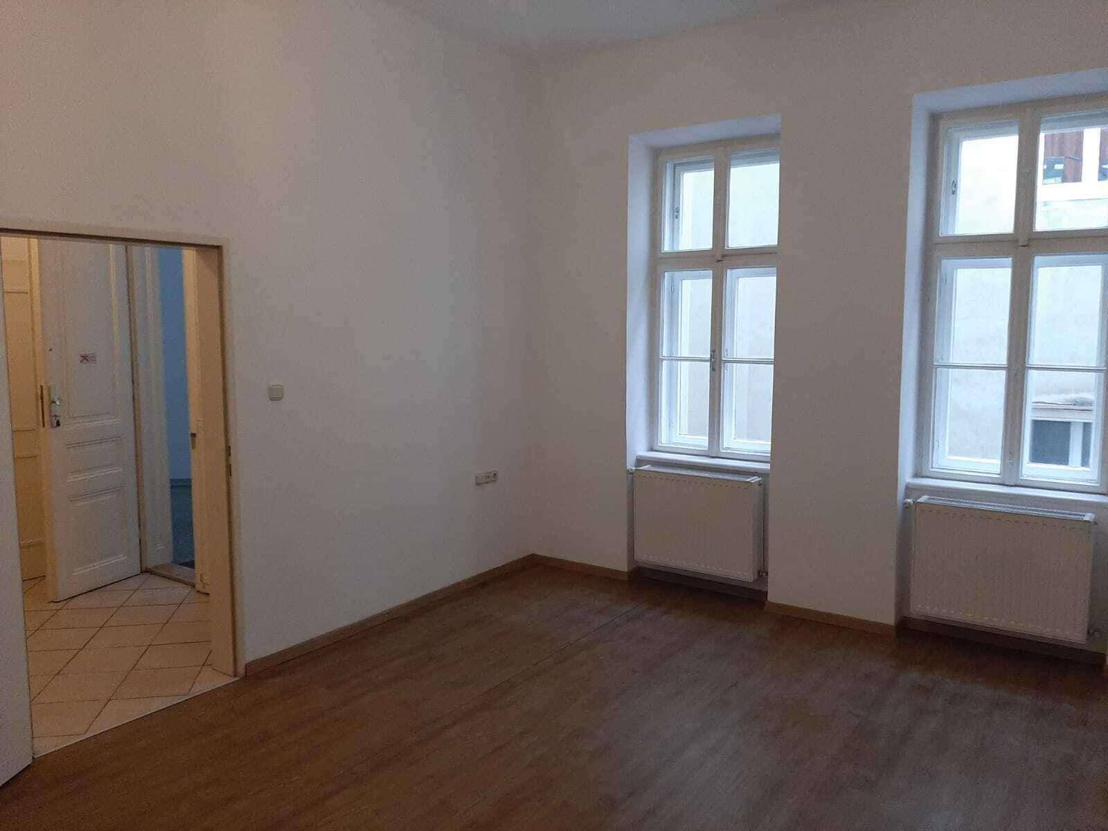 Geräumiges Zimmer mit Holzboden und Zugang zu einem gefliesten Bereich, ideal für Wohnzwecke.