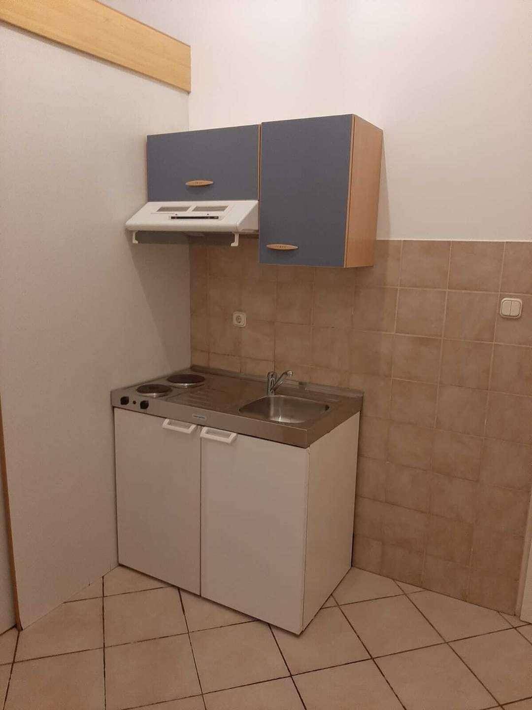 Funktionale Küchenzeile mit zwei Kochplatten, Spülbecken und Oberschränken, in gutem Zustand.