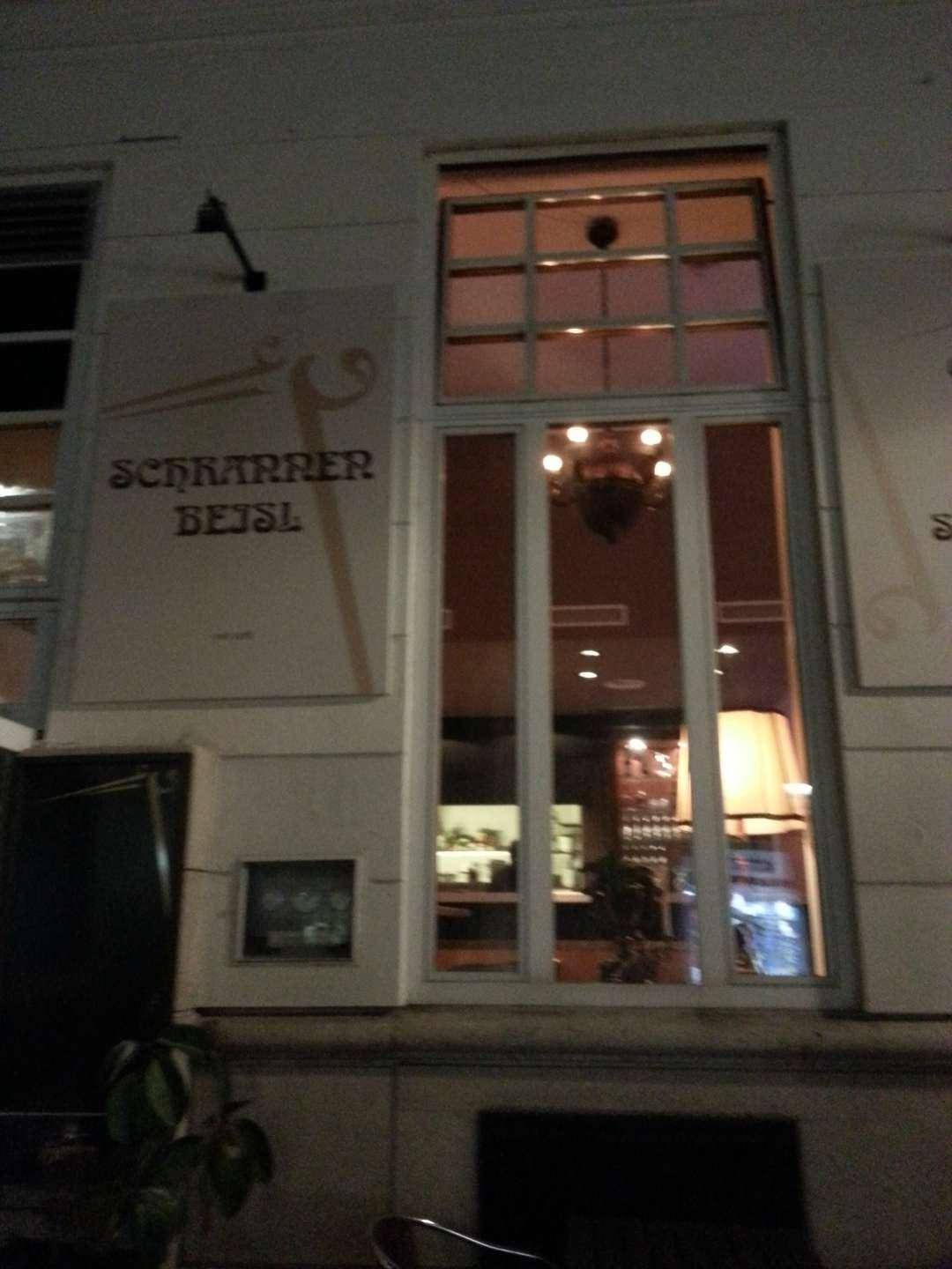 Fassade eines Cafés/Beisls bei Nacht mit beleuchteten Fenstern und Beschilderung.