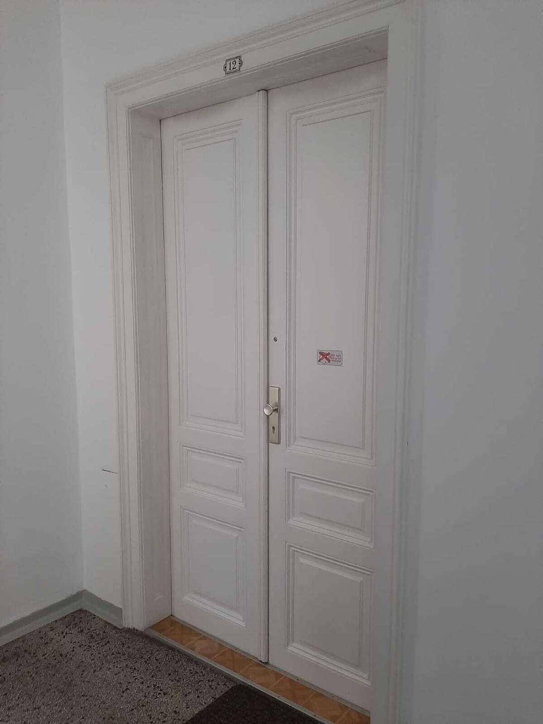 Weiße Doppeltür als Wohnungseingang mit der Nummer 12 in einem Altbau-Treppenhaus.