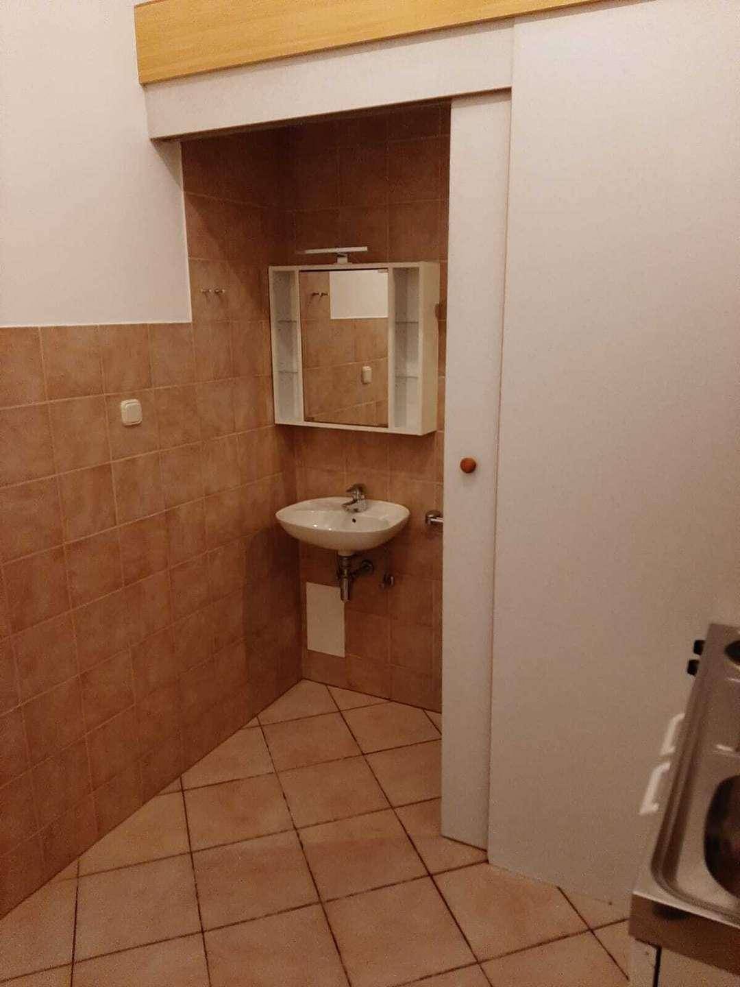 Kleines Badezimmer mit Waschbecken und Spiegelschrank, durch Schiebetür von der Küche zugänglich.