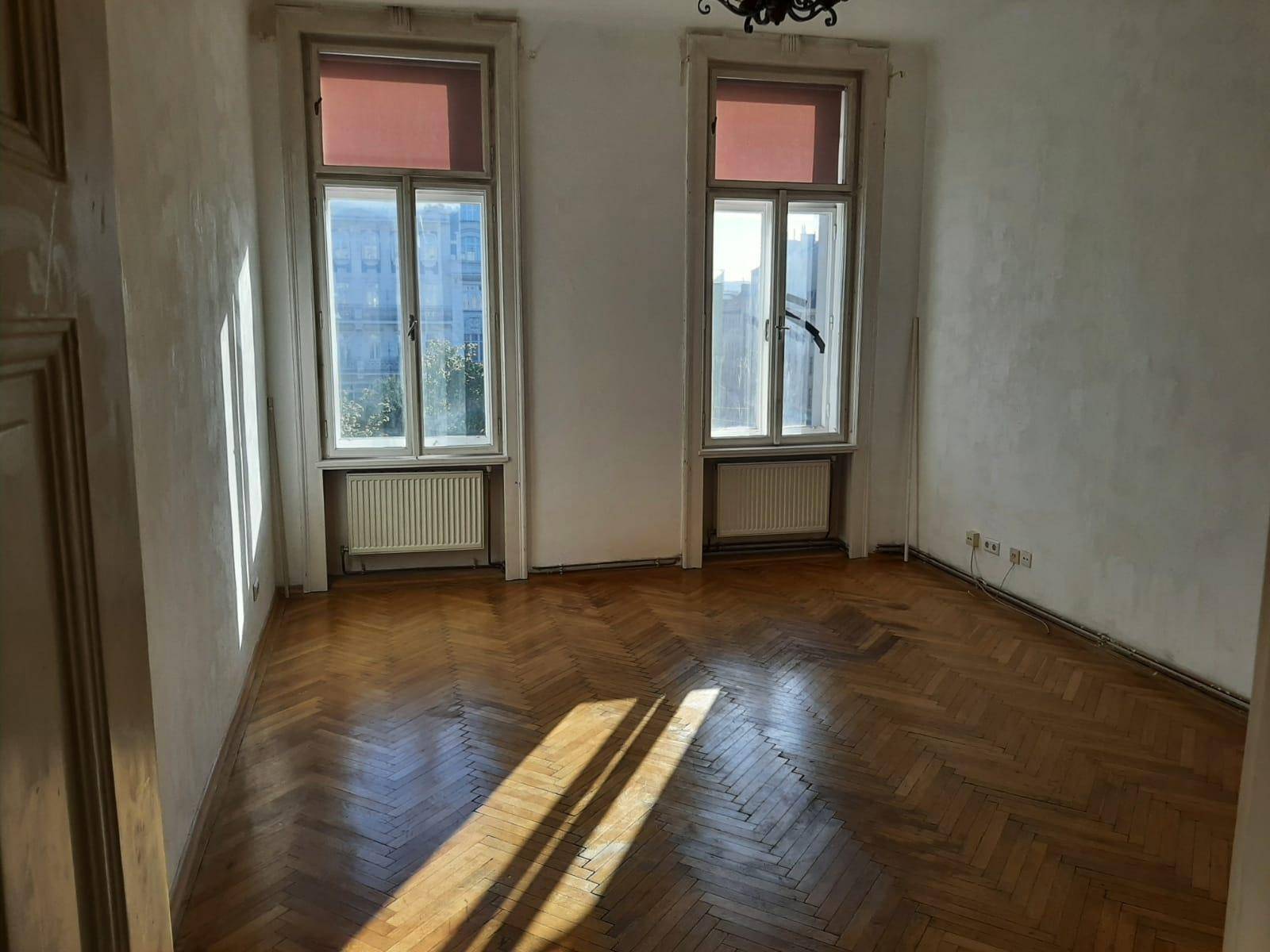 Geräumiges Zimmer mit klassischem Fischgrätparkett, zwei hohen Fenstern und viel Tageslichteinfall.