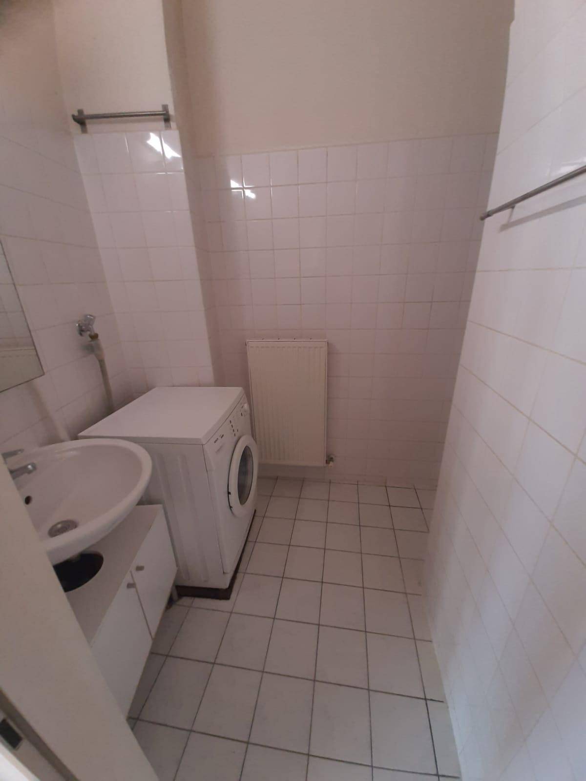 Schlichtes Badezimmer mit Waschbecken, Waschmaschine und weiß gefliesten Wänden, funktional und sauber.