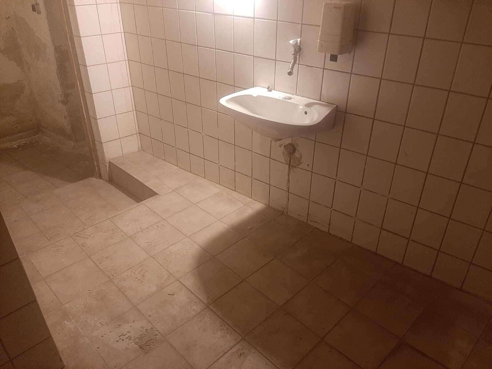 Einfacher Sanitärbereich mit gefliesten Wänden, Waschbecken und Seifenspender.