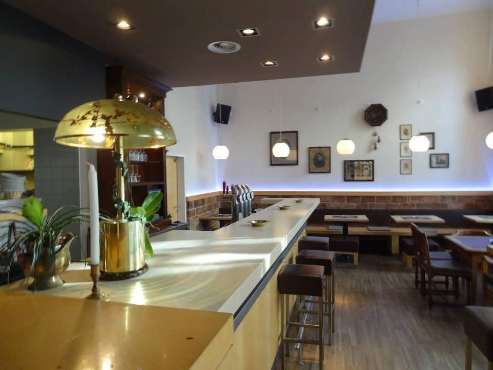 Innenansicht einer Bar oder eines Restaurants mit langer Theke, Sitzbänken und Holzboden.