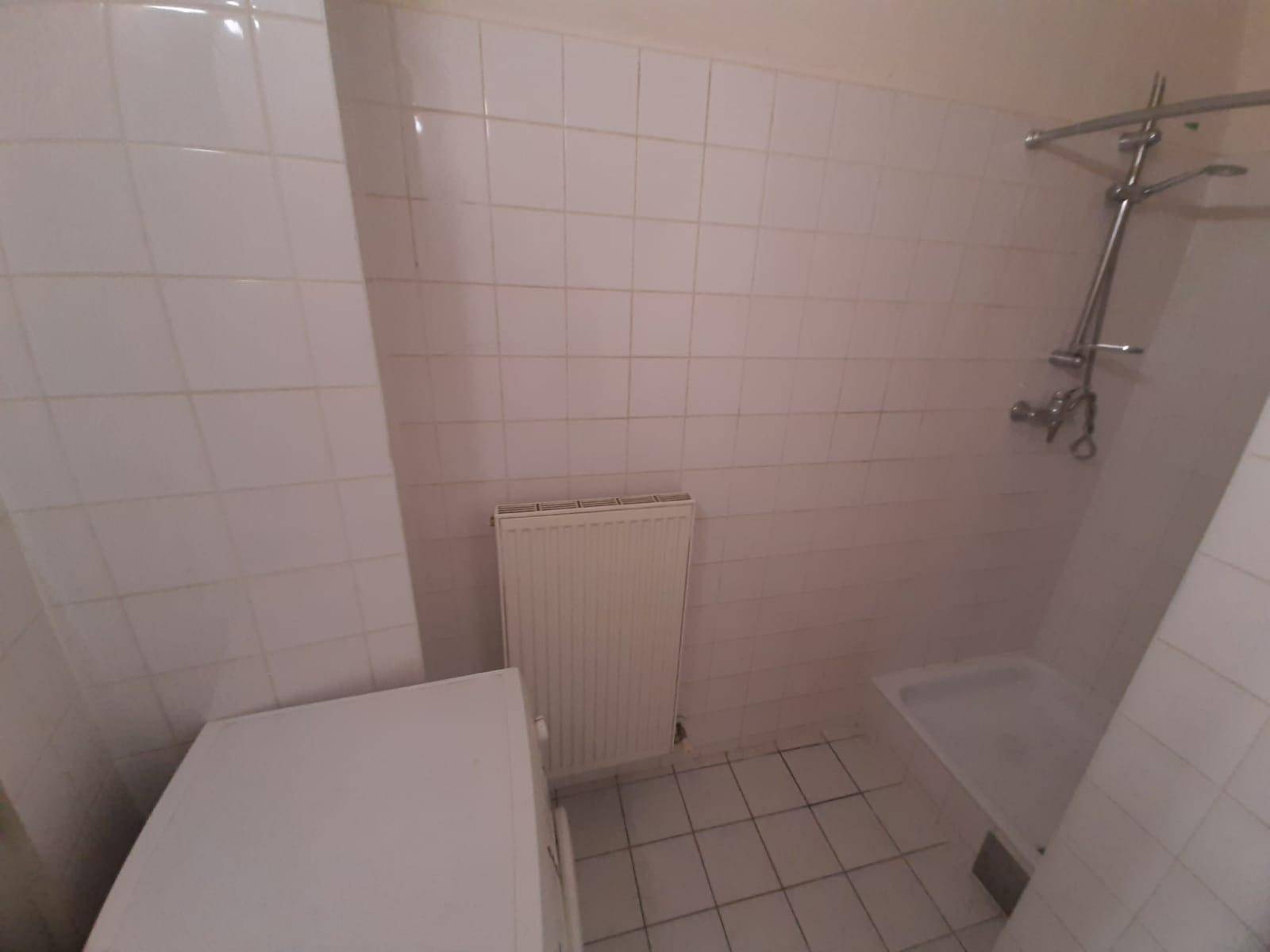 Badezimmer mit Duschbereich, Waschmaschine und Heizkörper an der Wand, komplett gefliest.