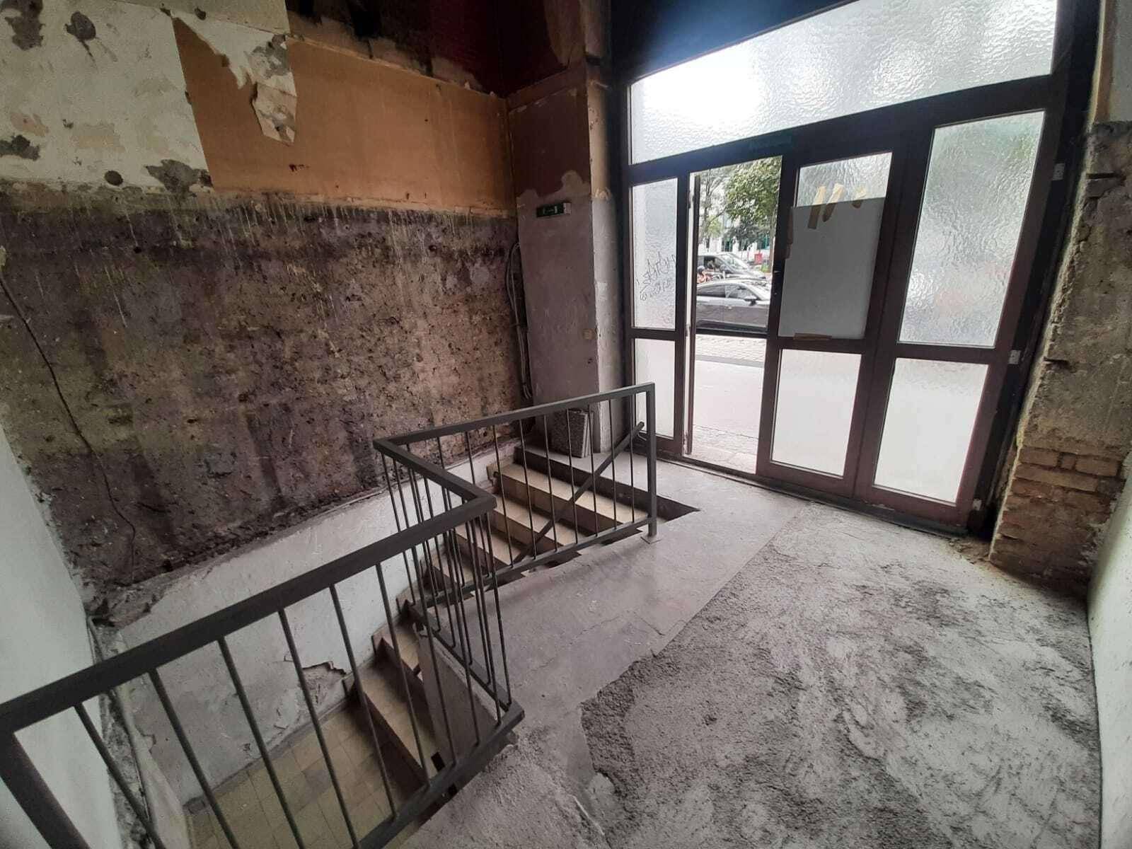 Treppenhaus im Rohzustand mit Blick auf die Eingangstür und die Straße, bereit zur Renovierung.