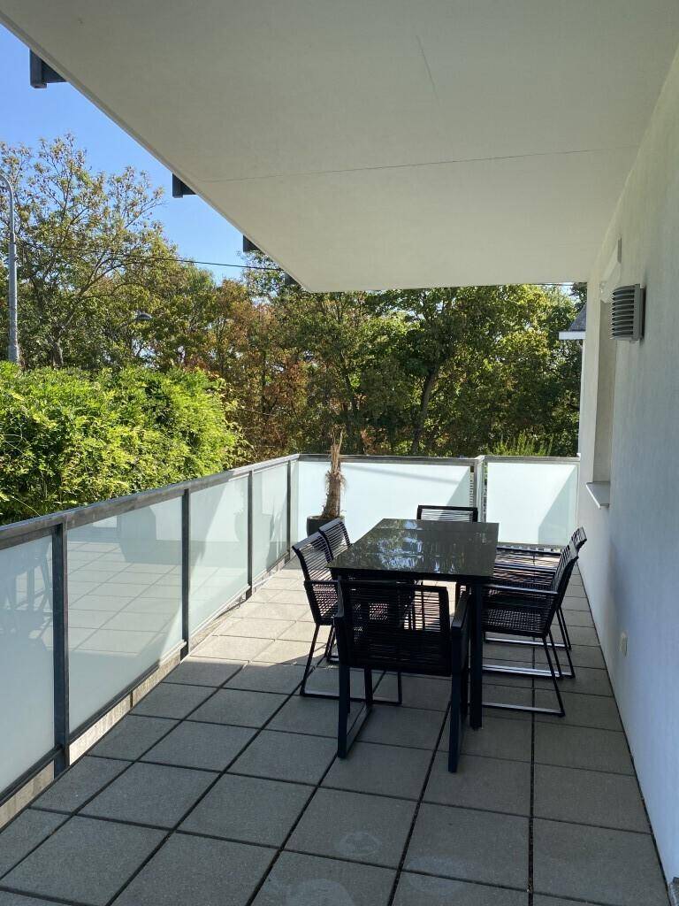 Heller und sonniger Balkon mit Fliesenboden, ausgestattet mit einem modernen Esstisch und Stühlen.