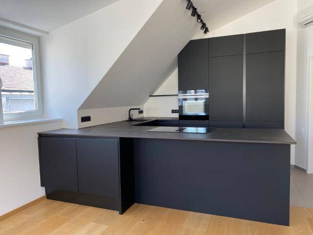 Elegante schwarze Küchenzeile mit integriertem Kochfeld und minimalistischem Design unter der Dachschräge.