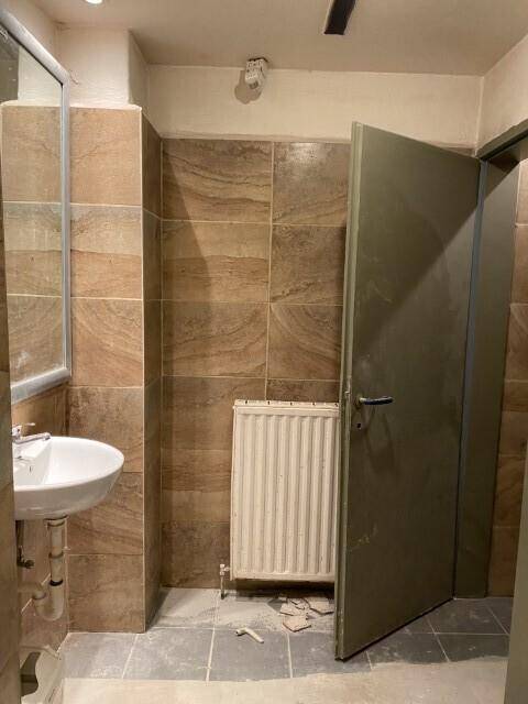 Waschraum mit Waschbecken, Heizkörper und braun gemusterten Wandfliesen, der eine Renovierung benötigt.