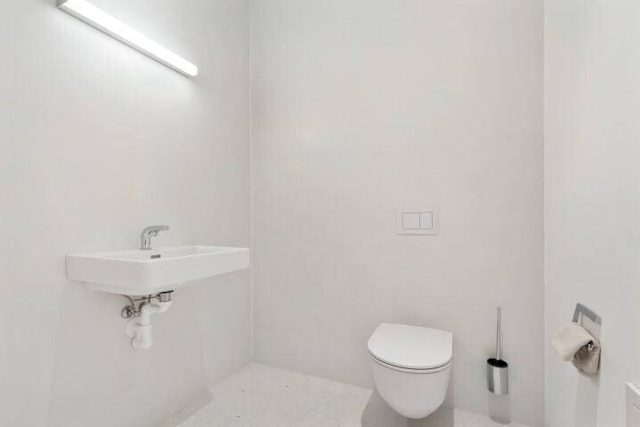 Schlichtes Gäste-WC mit wandhängender Toilette und kleinem Waschbecken, in minimalistischem Stil.