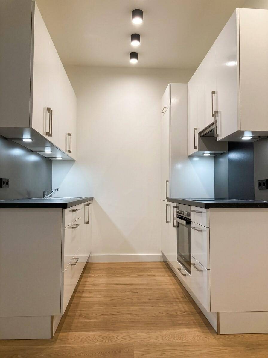 Schmale, moderne Küche mit weißen Schränken, dunklen Arbeitsplatten und integrierten Geräten.