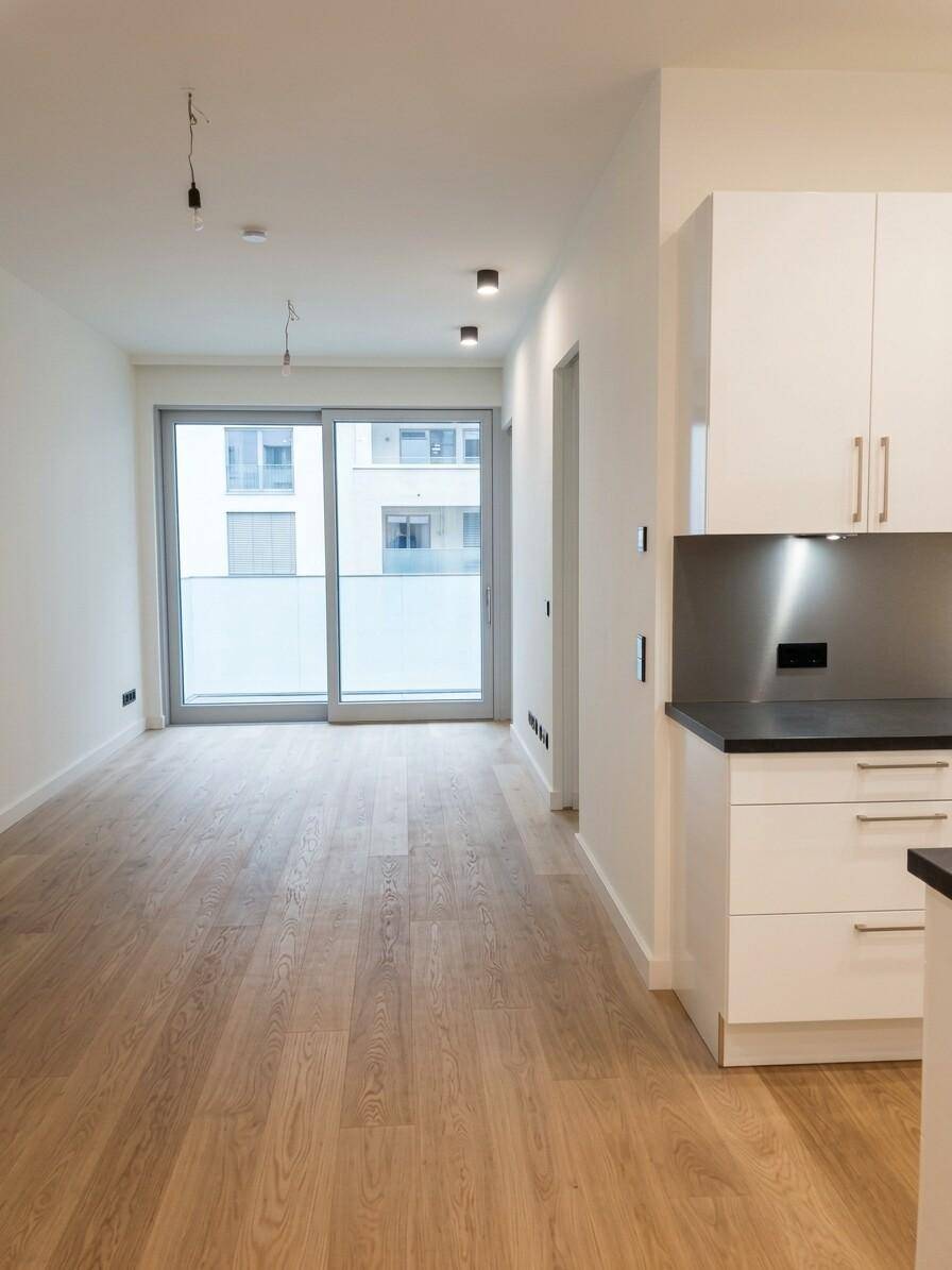 Offener Wohnbereich mit integrierter Küchenzeile, Holzboden und Zugang zum Balkon.