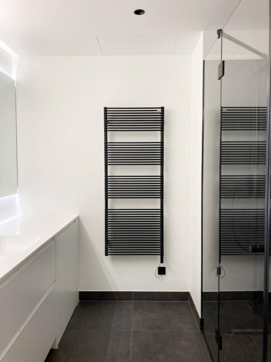 Elegantes Badezimmer mit begehbarer Dusche, beheiztem Handtuchhalter und dunklen Bodenfliesen.
