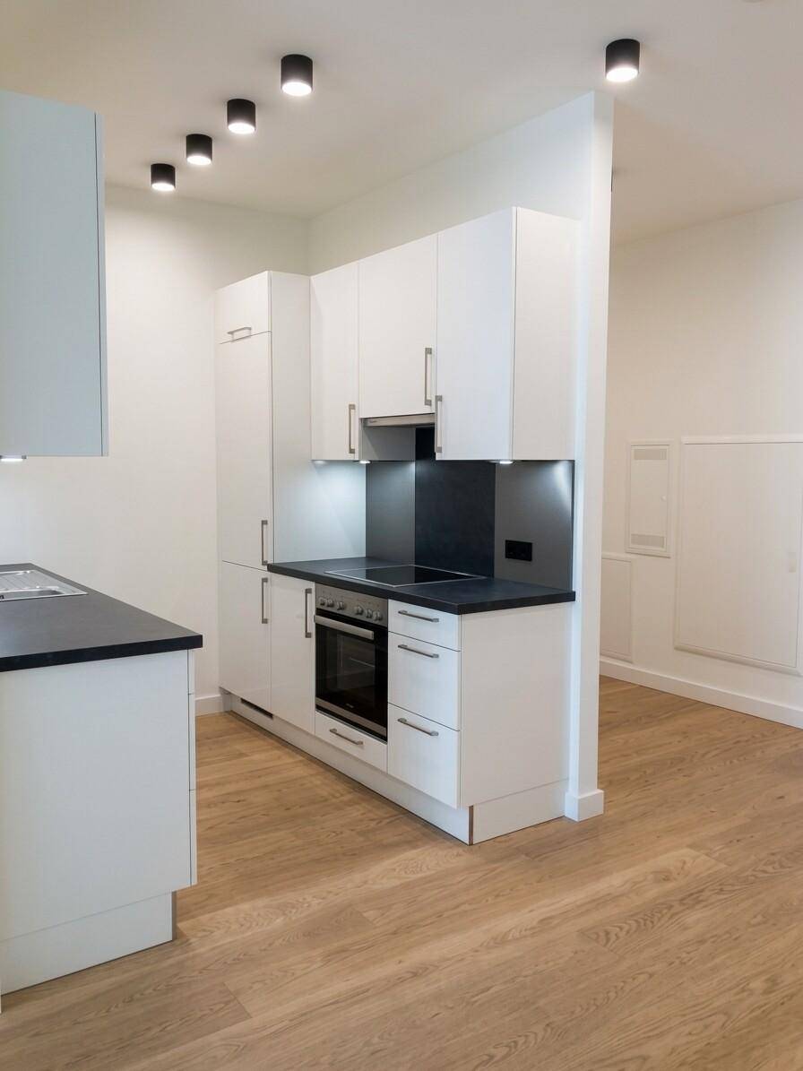 Moderne Einbauküche mit weißen Schränken, dunkler Arbeitsplatte und integrierten Geräten.