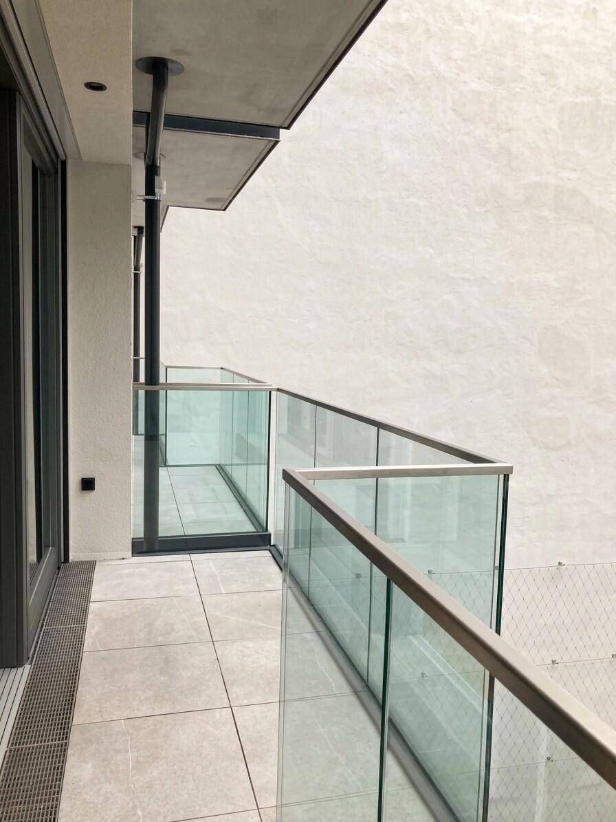 Moderner Balkon mit Glasgeländer und Fliesenboden, der einen Blick auf die Umgebung bietet.