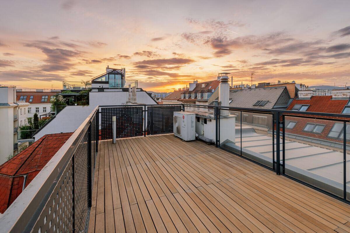 Dachterrasse mit Holzdeck und Glasgeländer bietet einen atemberaubenden Blick auf den Sonnenuntergang über der Stadt.