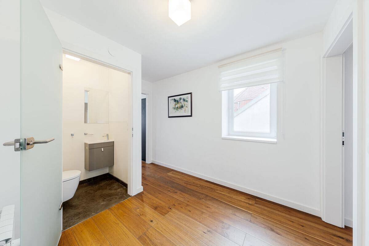 Helles Schlafzimmer mit Holzboden und Fenster, angrenzend an ein kleines Badezimmer mit WC.