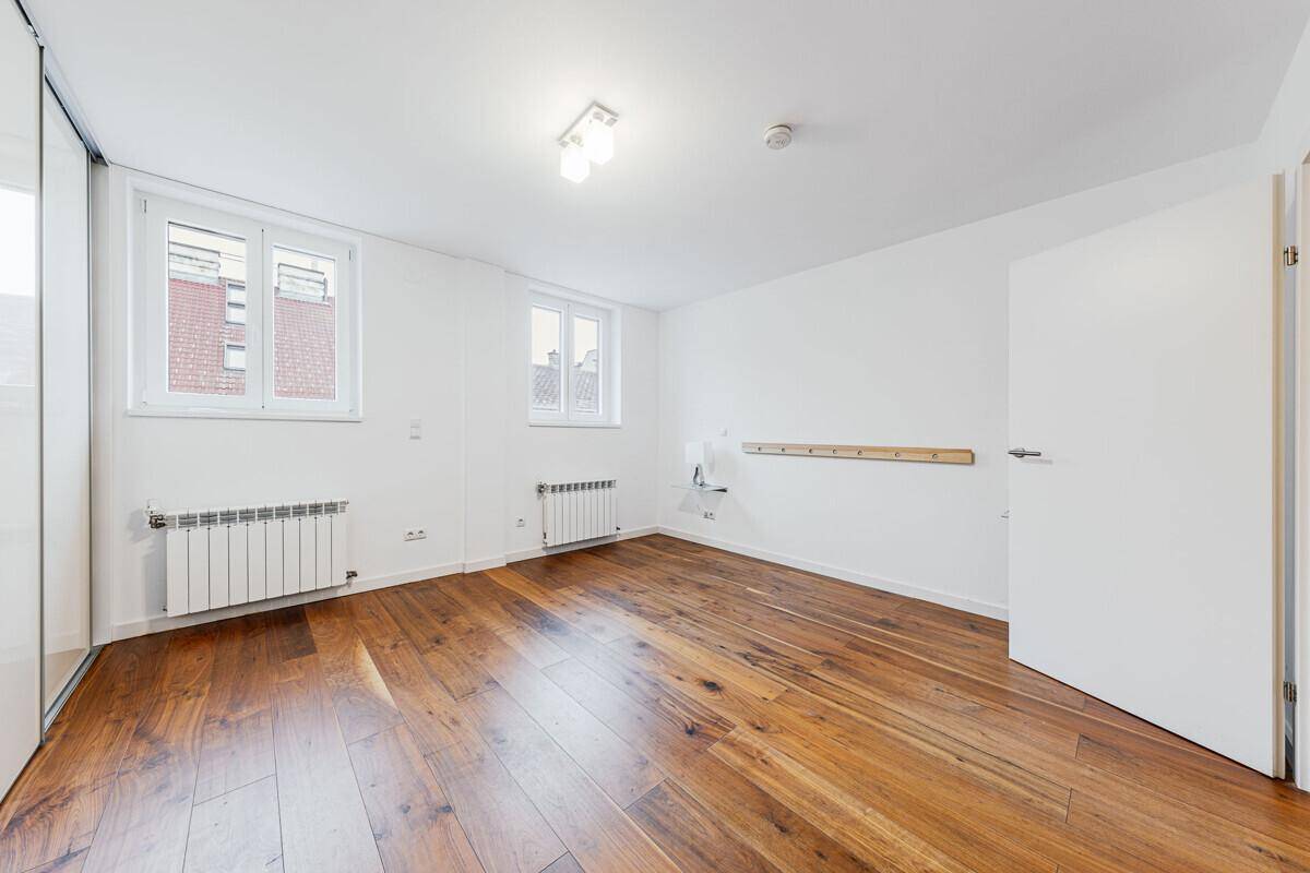 Helles Schlafzimmer mit Holzboden, zwei Fenstern und Heizkörpern, ideal für individuelle Gestaltung.