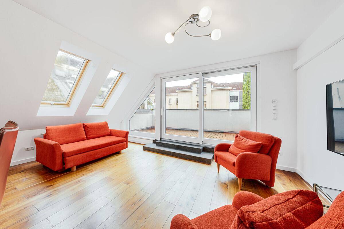 Lichtdurchflutetes Wohnzimmer mit roten Sofas, Holzboden und Zugang zu einem sonnigen Balkon.