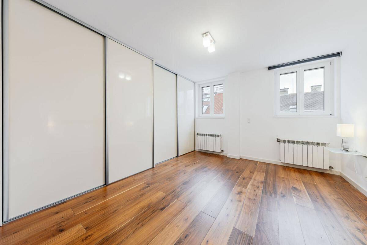 Schlafzimmer mit Holzboden, weißen Schiebetürenschränken und zwei Fenstern für viel Tageslicht.