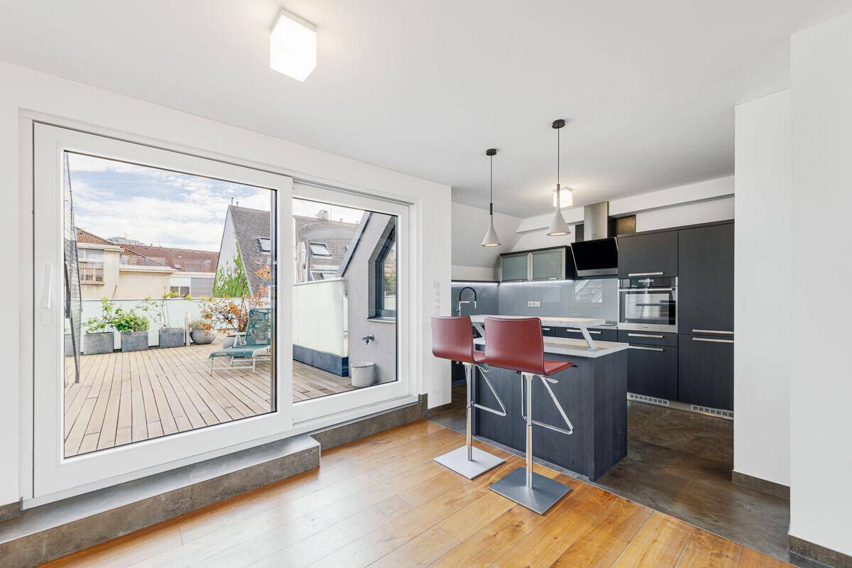 Moderne offene Küche mit Kücheninsel und Barhockern, direktem Zugang zur sonnigen Dachterrasse.