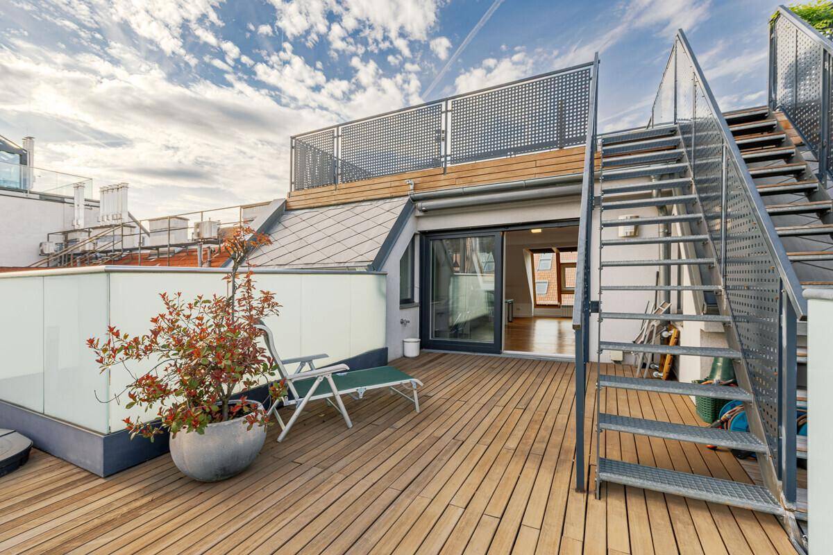 Mehrstufige Dachterrasse mit Holzdeck, Metalltreppe und Liegestuhl für entspannte Stunden im Freien.