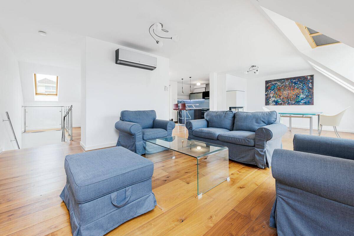 Offener Wohnbereich mit bequemen blauen Sofas, Glastisch und Blick auf die Küche und Treppe.