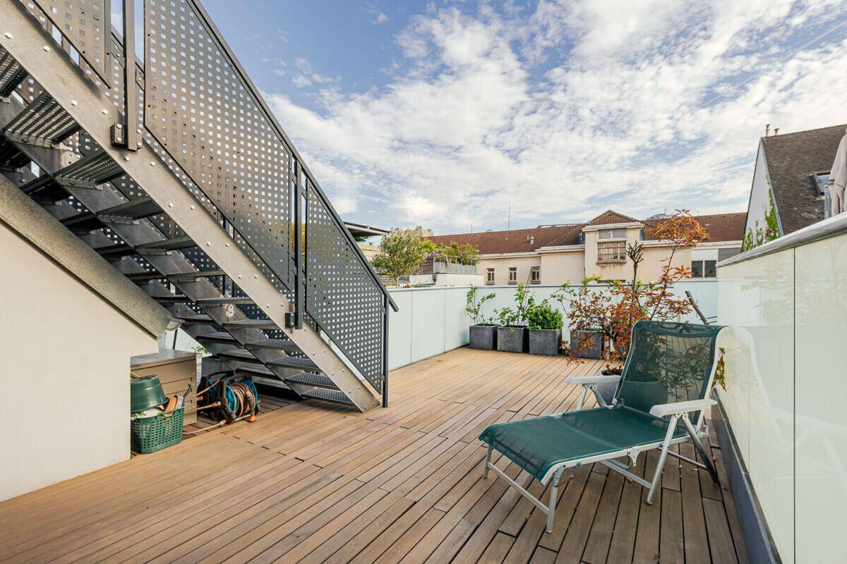 Teil der Dachterrasse mit Holzbelag, einer Sonnenliege und einer Metalltreppe zum oberen Bereich.